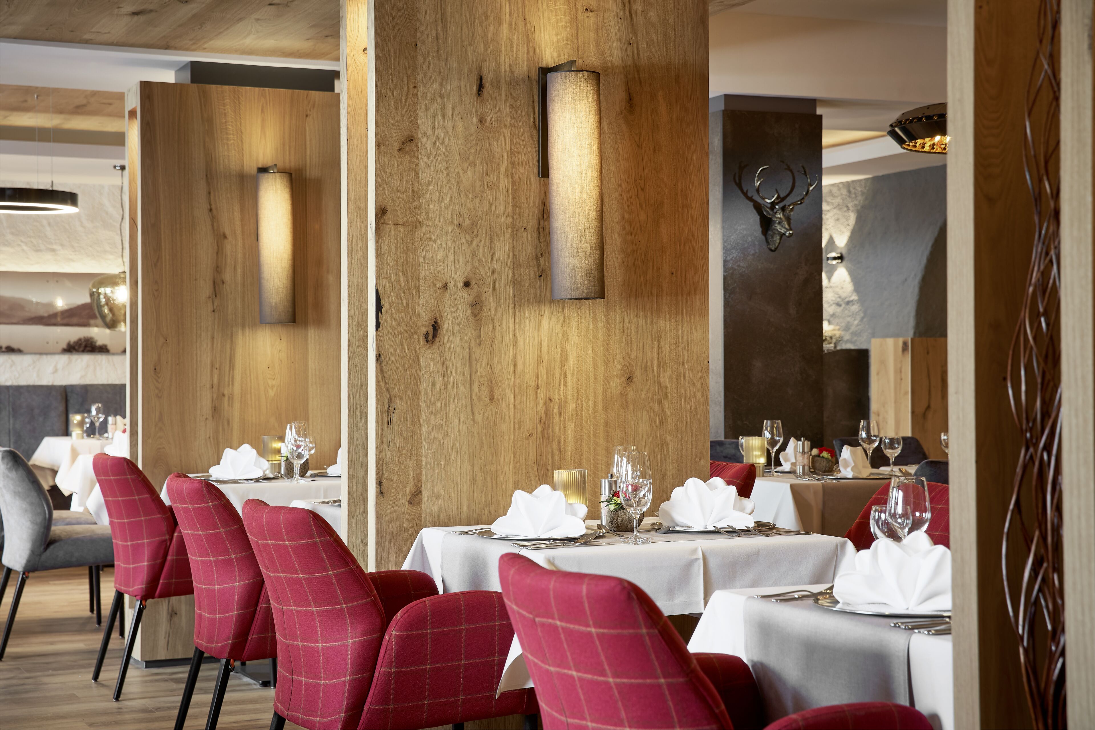 A restaurant with wooden panel walls, red upholstered chairs, and white tablecloths.