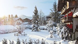 Een besneeuwde plaats met traditionele houten huizen, een met sneeuw bedekte boom en een houten bank.