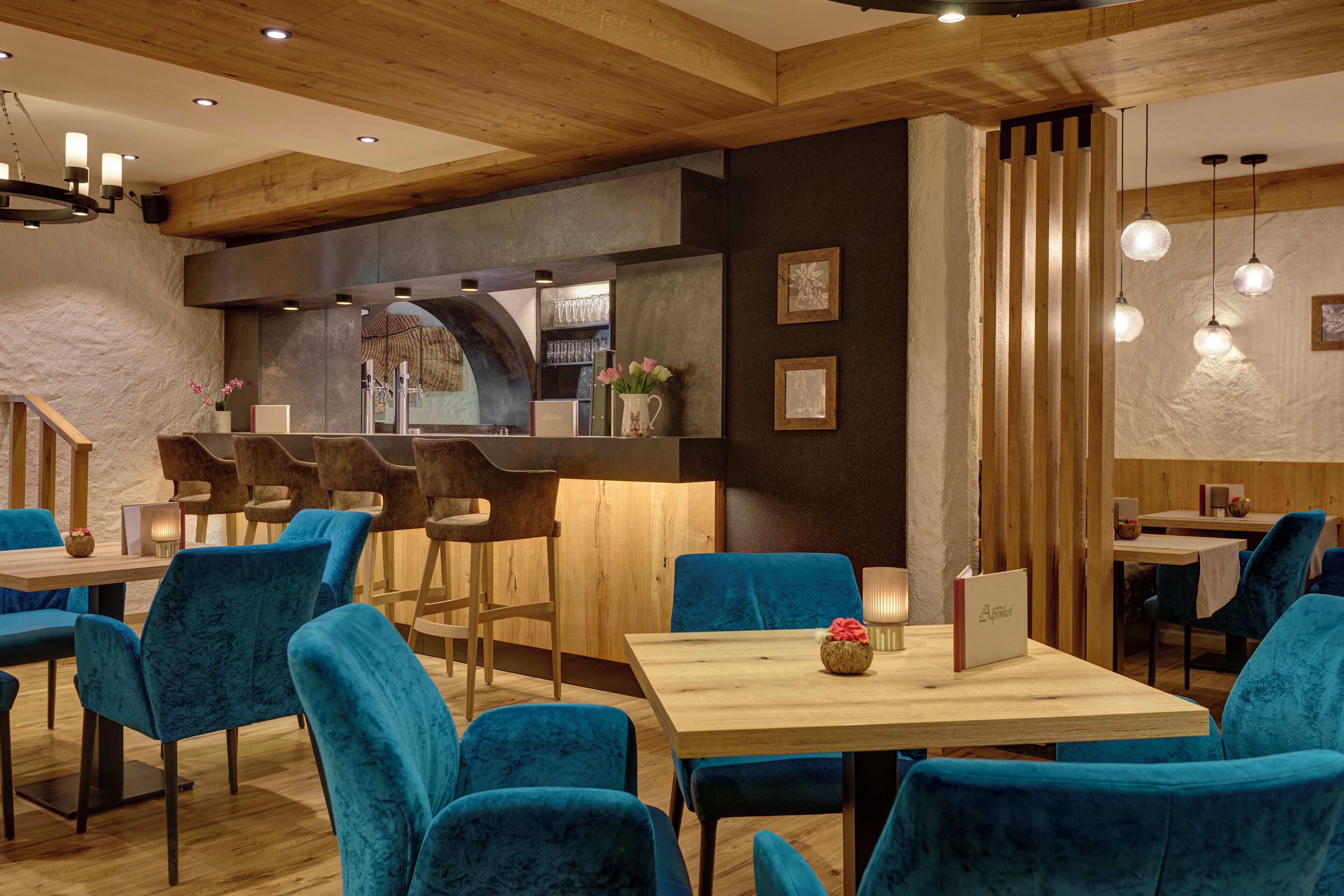 A restaurant interior with wooden beams, blue velvet chairs, and a bar area.