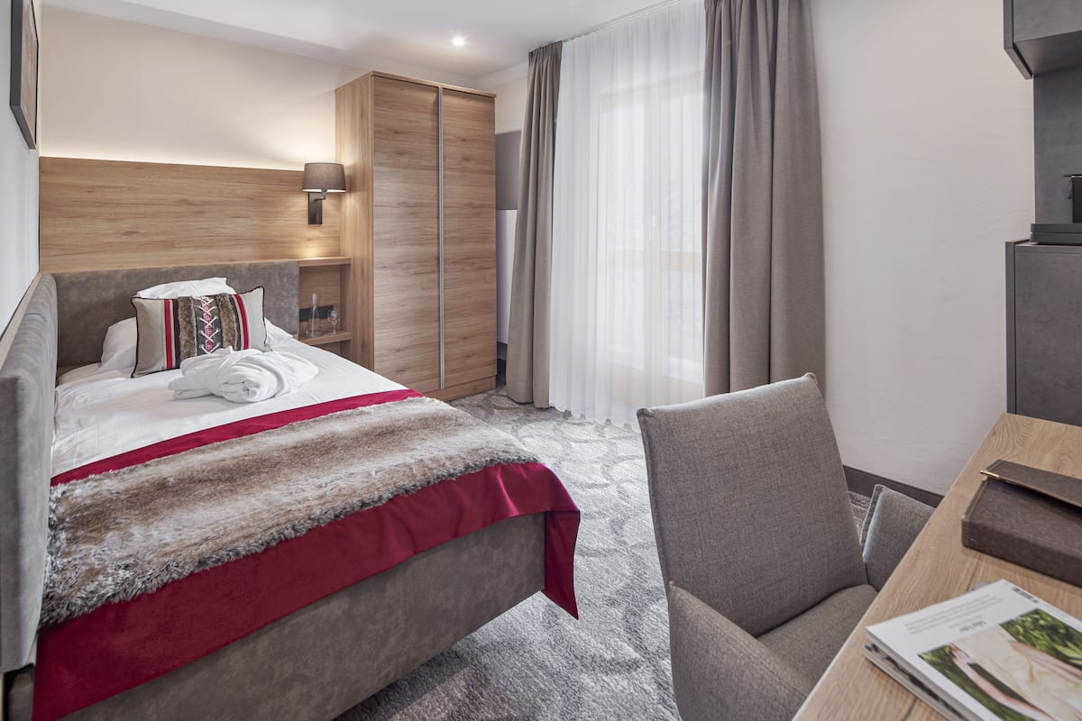 Ein modernes Hotelzimmer mit Bett, Schreibtisch, Stuhl, Kleiderschrank und einem fenster mit Vorhängen.
