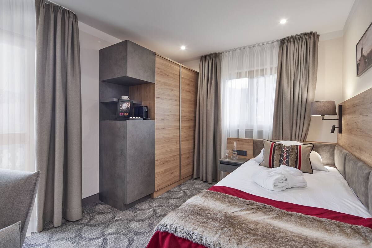 Ein Hotelzimmer mit Bett, Kleiderschrank, Schreibtisch mit Kaffeemaschine und Vorhängen.