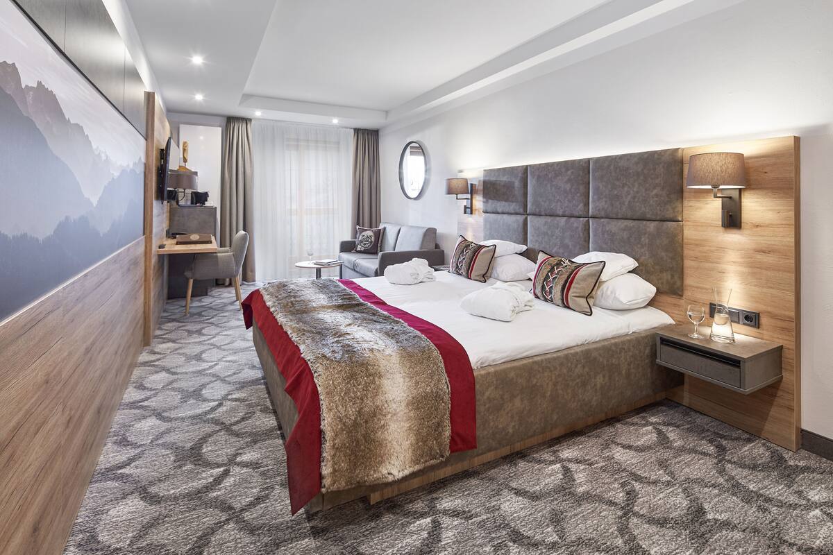 Ein modernes Hotelzimmer mit einem großen Bett, einem Schreibtisch, einem Sessel und einem Fernseher.
