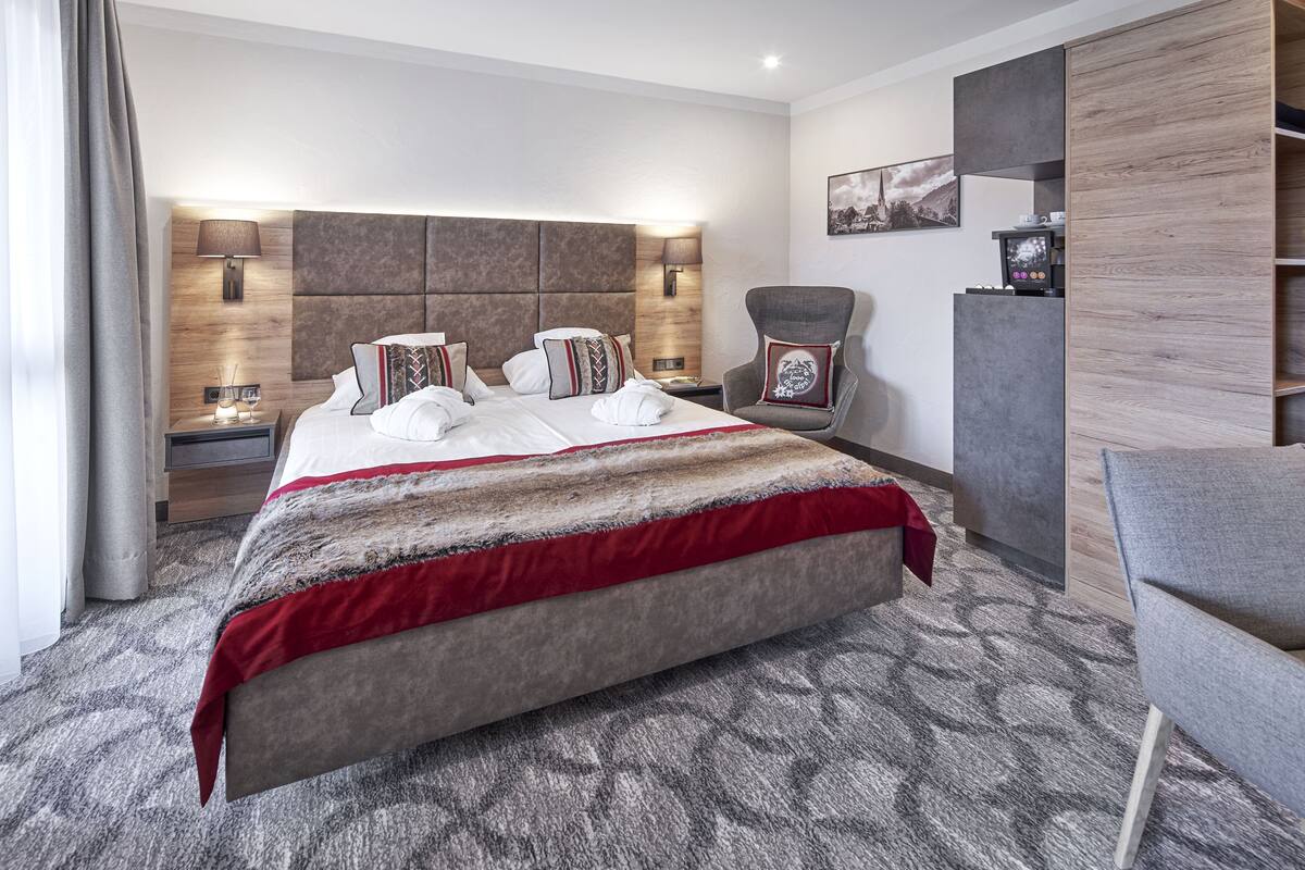 Ein modernes Hotelzimmer mit einem großen Bett, einem Sessel, einem Schreibtisch und einer Kaffeemaschine.