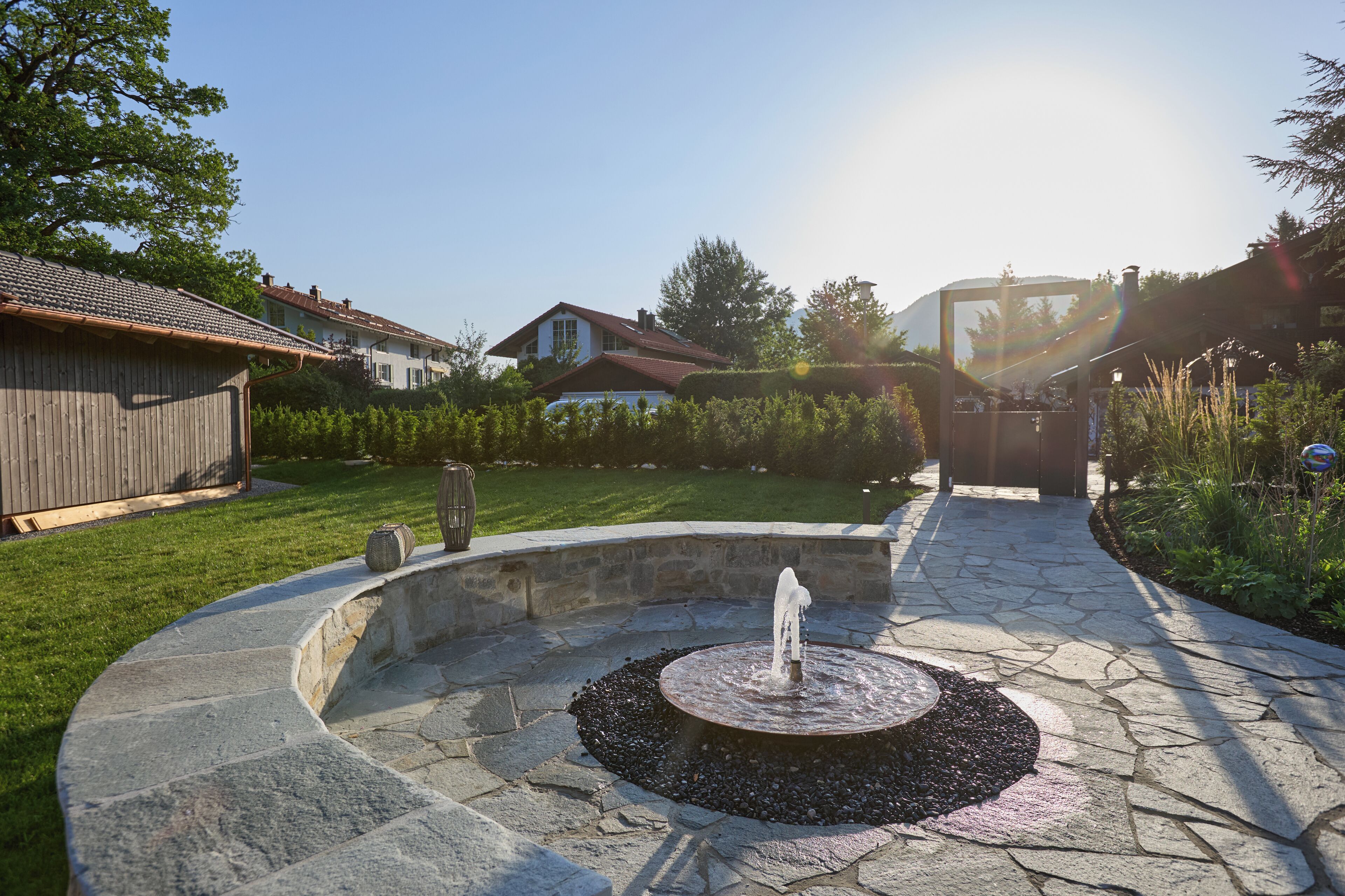 A stone fountain in a circular stone basin with a clear sky and houses in the background.