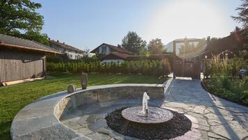 A stone fountain in a circular stone basin with a clear sky and houses in the background.