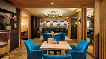 A modern interior with a wooden ceiling, a central dining table surrounded by blue chairs, and a kitchen area in the background.