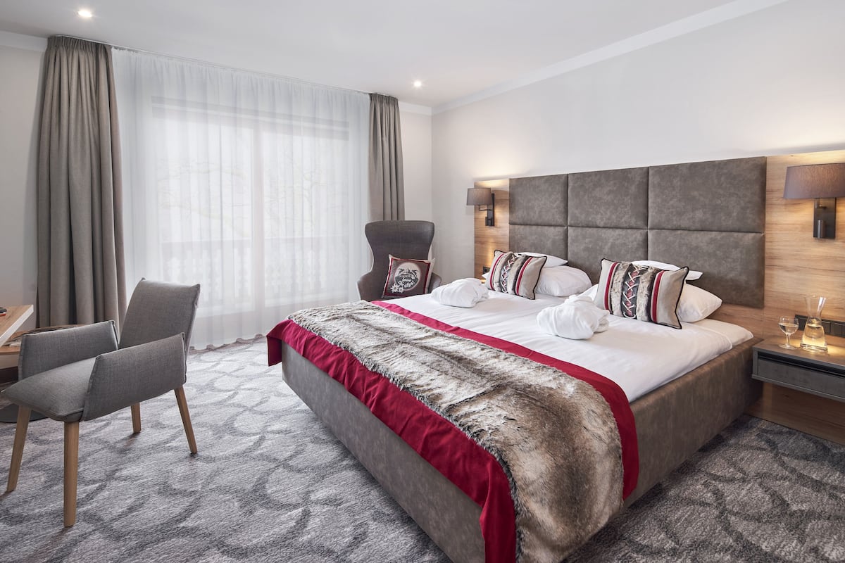 Ein modernes Hotelzimmer mit einem großen Bett, einem Sessel, einem Schreibtisch und einem Nachttisch mit Lampe.