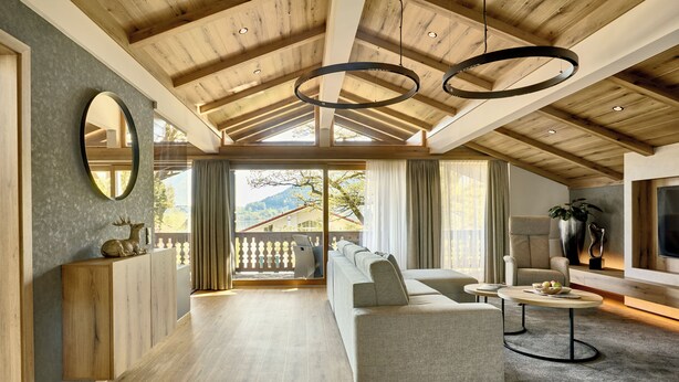 Een ruime woonkamer met een hoge plafond, houten balken, een grote bank, een televisie en een balkon met uitzicht op de omgeving.