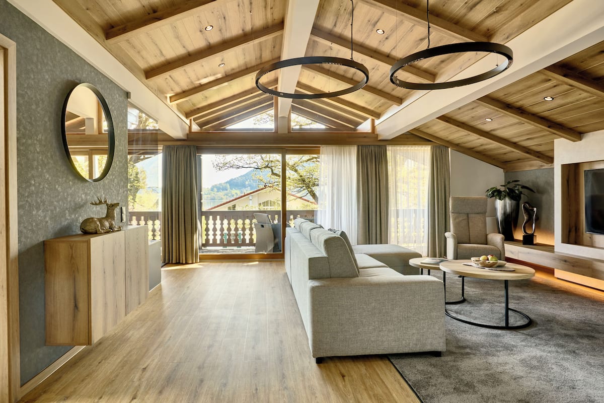 Ein großzügiger Wohnbereich mit hoher Decke, Holzbalken, einem großen Sofa, einem Fernseher und einem Balkon mit Blick ins Freie.