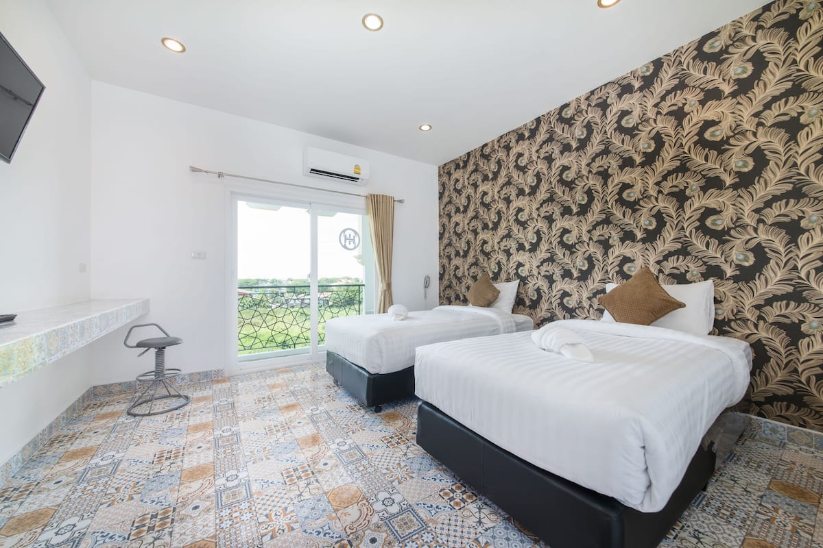 A hotel room with two beds, a small desk, and a balcony with a view.