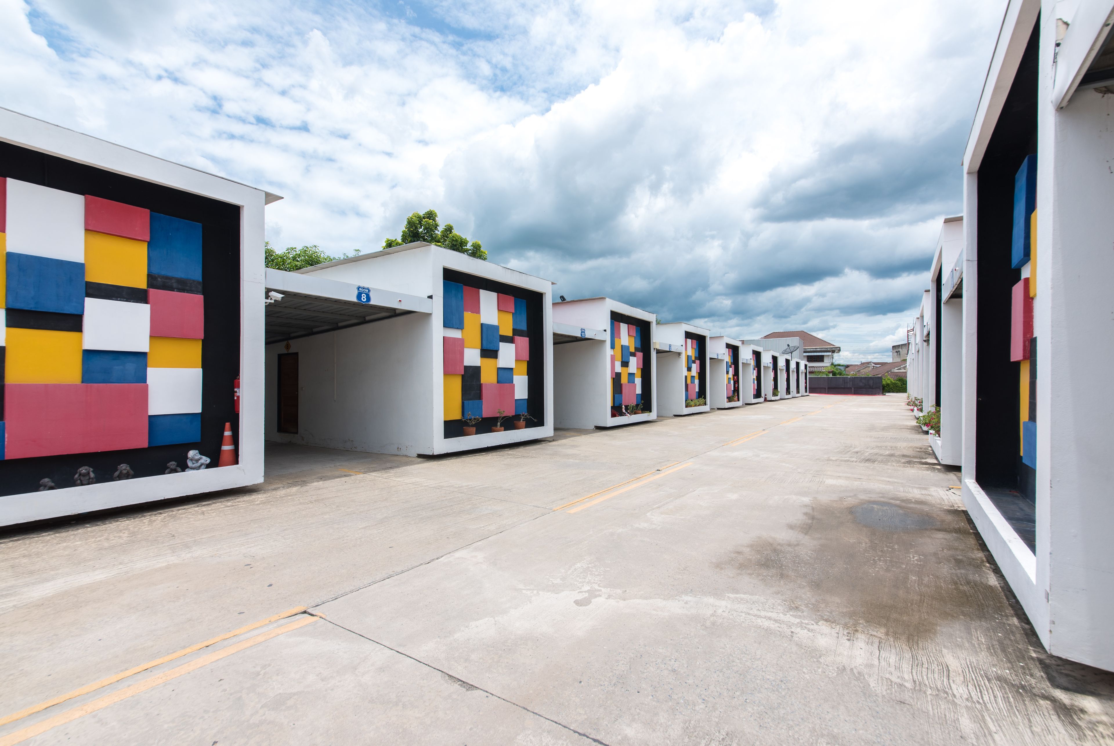 A row of modern, white buildings with colorful geometric patterns on the facades, arranged in a linear fashion with a clear pathway in between.