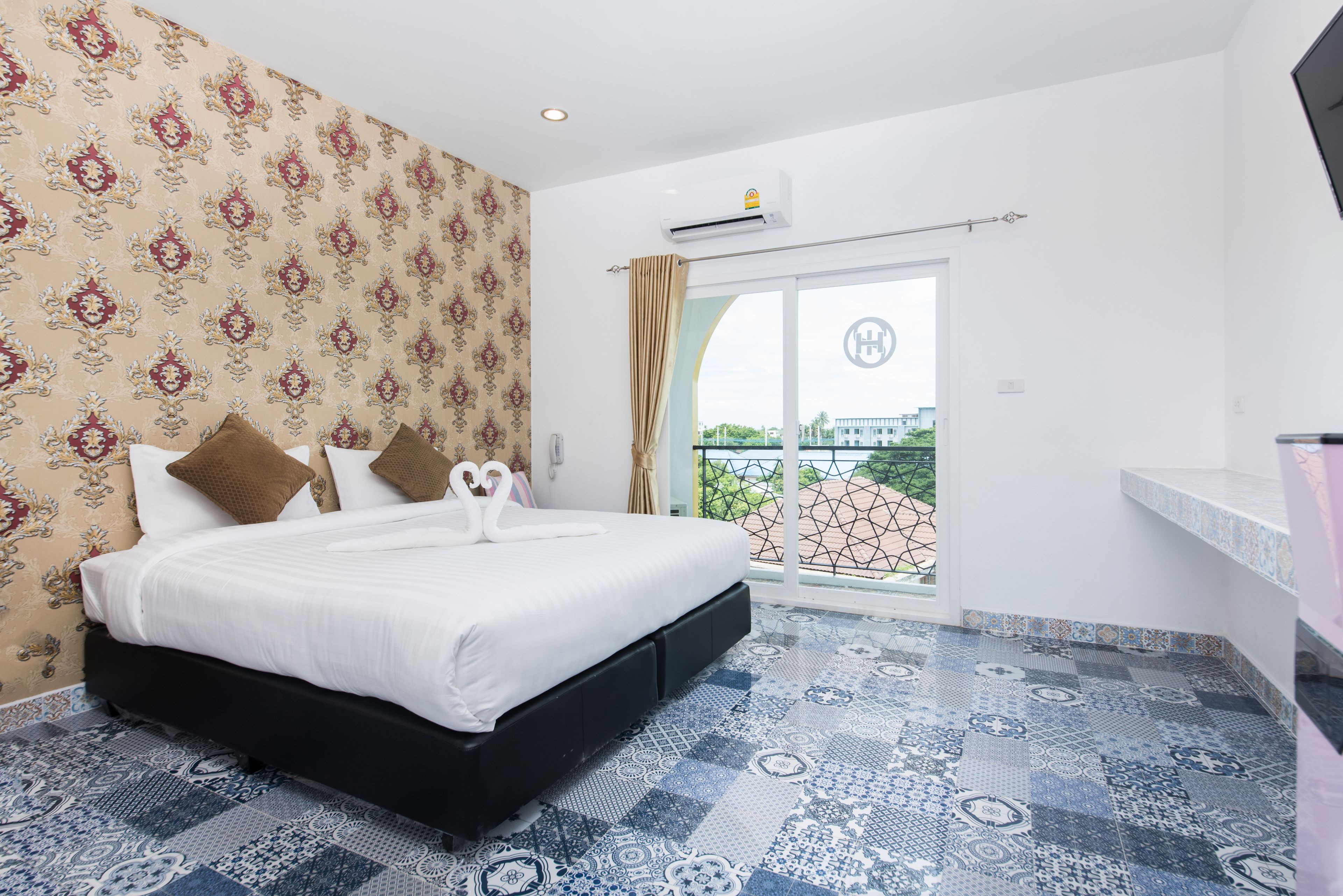 A bedroom with a bed, patterned wallpaper, a view through a glass door, and a tiled floor.