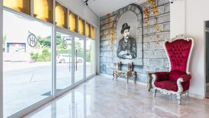 A spacious lobby with a large glass door, a red velvet armchair, and a stone wall mural. - Oasis Hiso Hotel (Lop Buri)