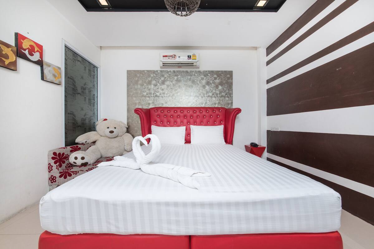 A neatly made bed with a red headboard, a teddy bear, and a towel shaped like a swan on the bed.