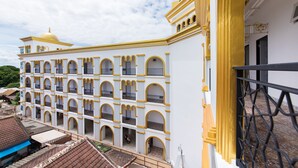 A multi-story building with a white facade and yellow accents, featuring balconies and a dome structure. - Oasis Hiso Hotel (Lop Buri)