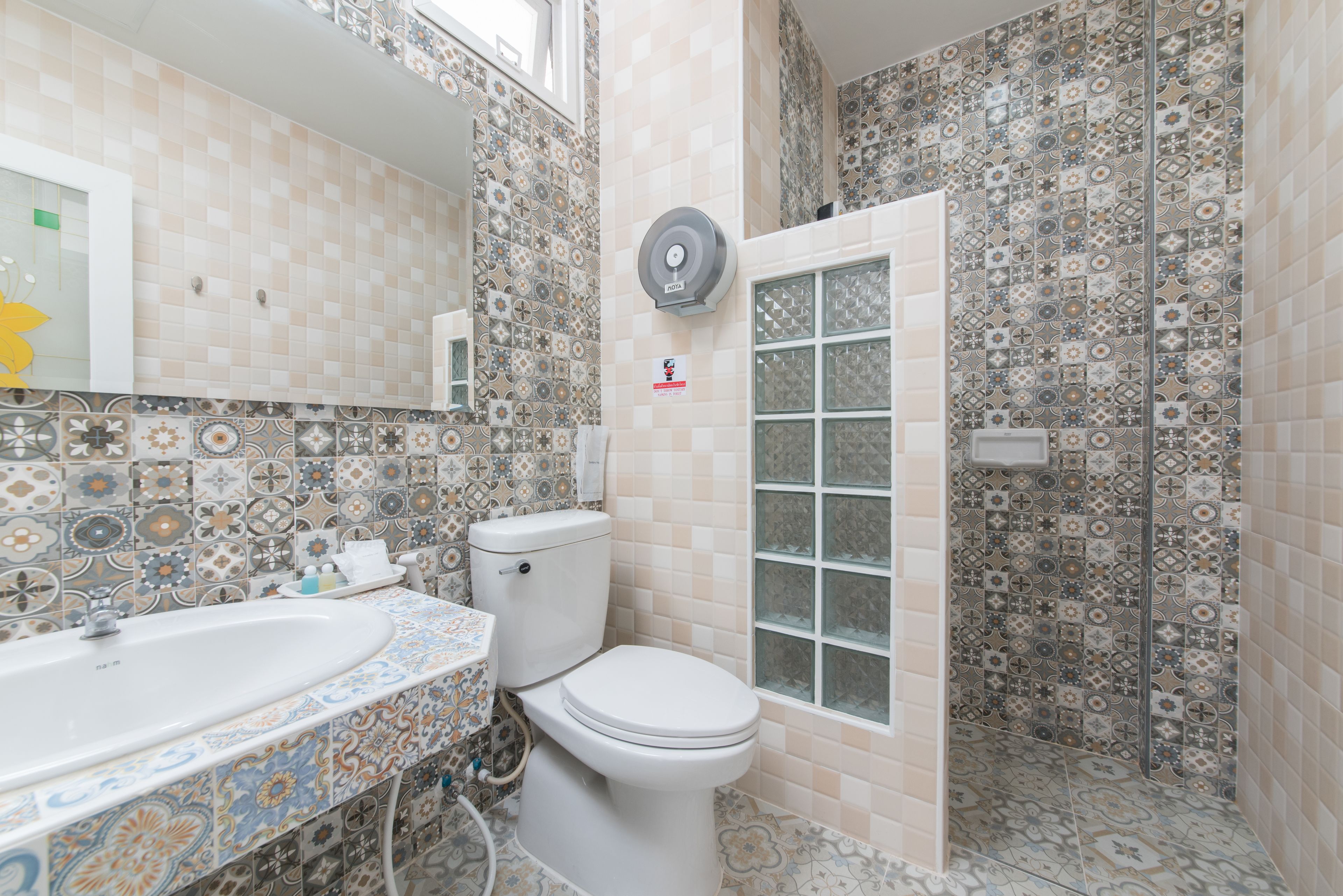 Un bany amb dutxa revestida de rajoles, un vàter i un lavabo amb un respatller decoratiu.