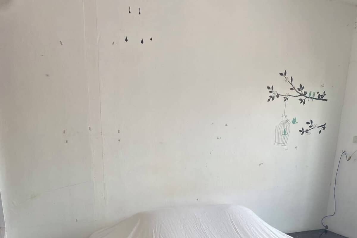 A single bed with a white mattress and a swan-shaped towel on it, in a room with dark marble flooring and a white wall with a small branch and bird decoration.