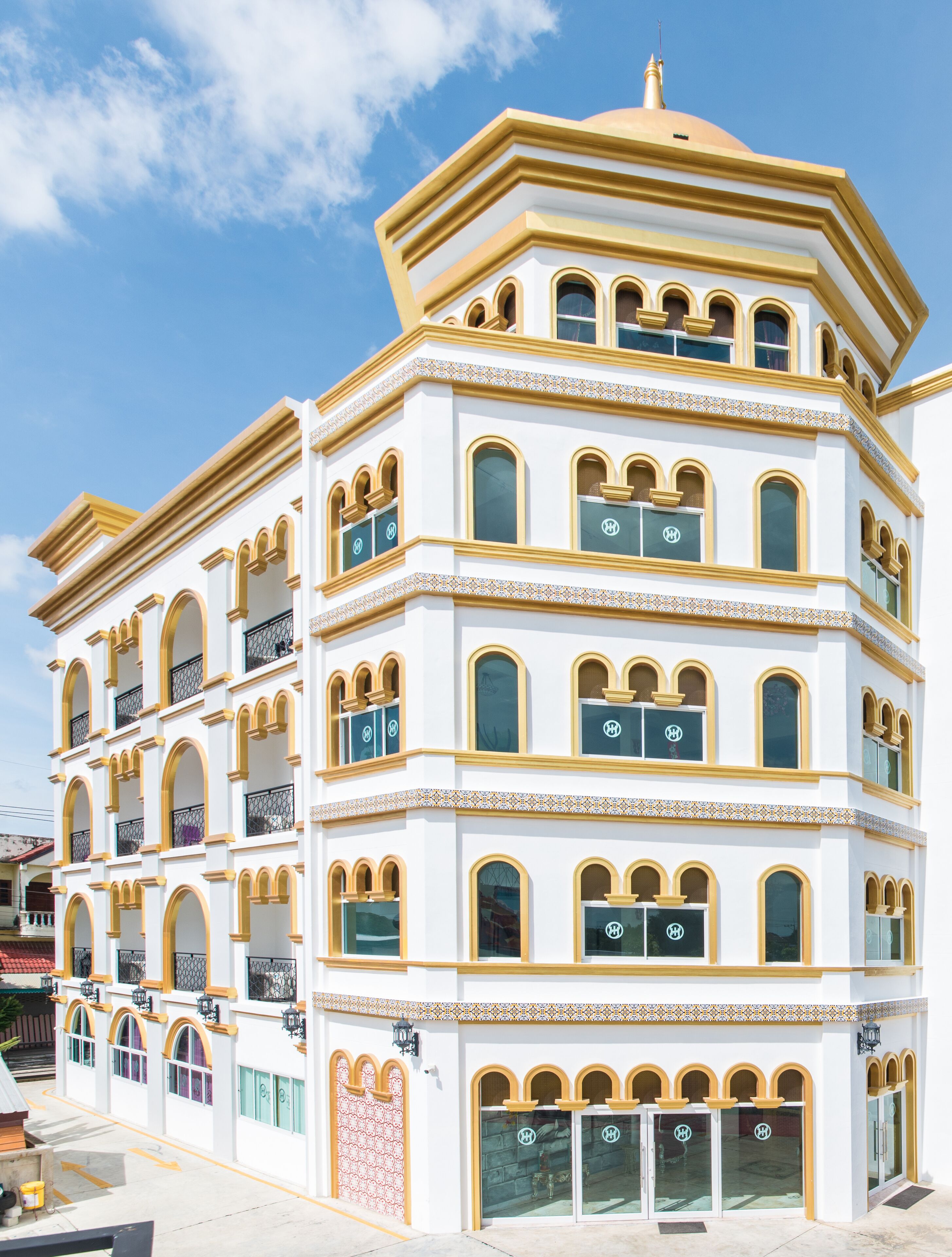 A multi-story building with a white facade and gold trim, featuring multiple balconies and arched windows.