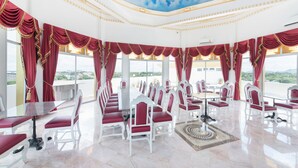 A banquet hall with a long table, red curtains, and a view of the city. - Oasis Hiso Hotel (Lop Buri)