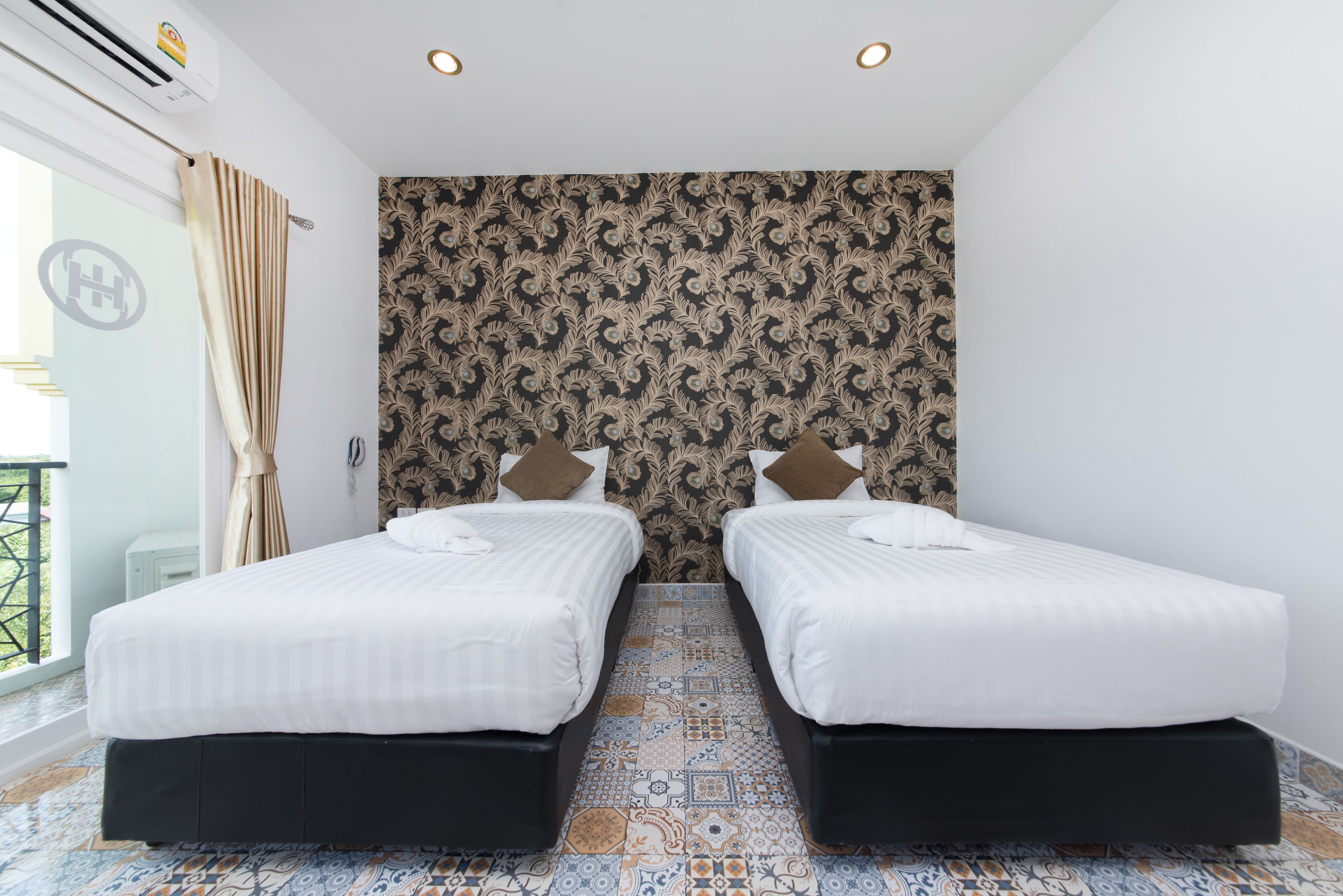 Une chambre d’hôtel avec deux lits, un papier peint à motifs, un sol carrelé et un balcon avec vue.