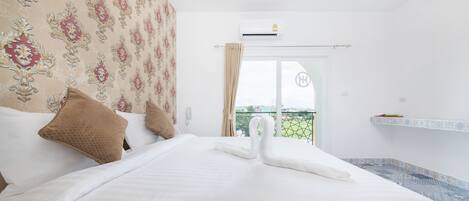 A hotel room with a large bed, a balcony with a view, and an air conditioning unit.