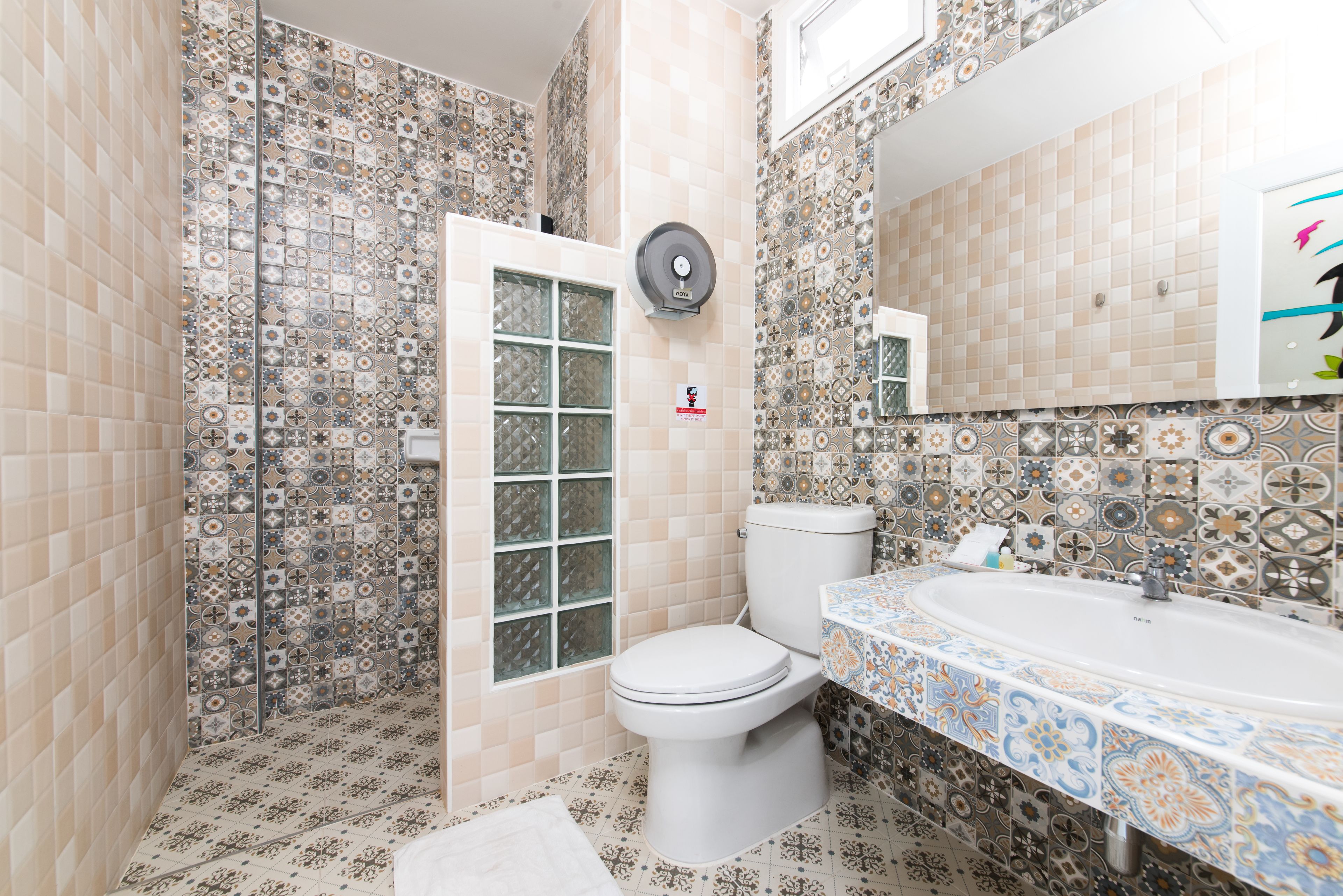 A bathroom with patterned tiles, a toilet, a sink, and a window.