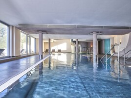 Una piscina interior con agua cristalina, iluminada por grandes ventanales, y vistas a un paisaje montañoso.