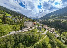 A town with a prominent hotel featuring multiple floors, a church, and a mountainous backdrop.