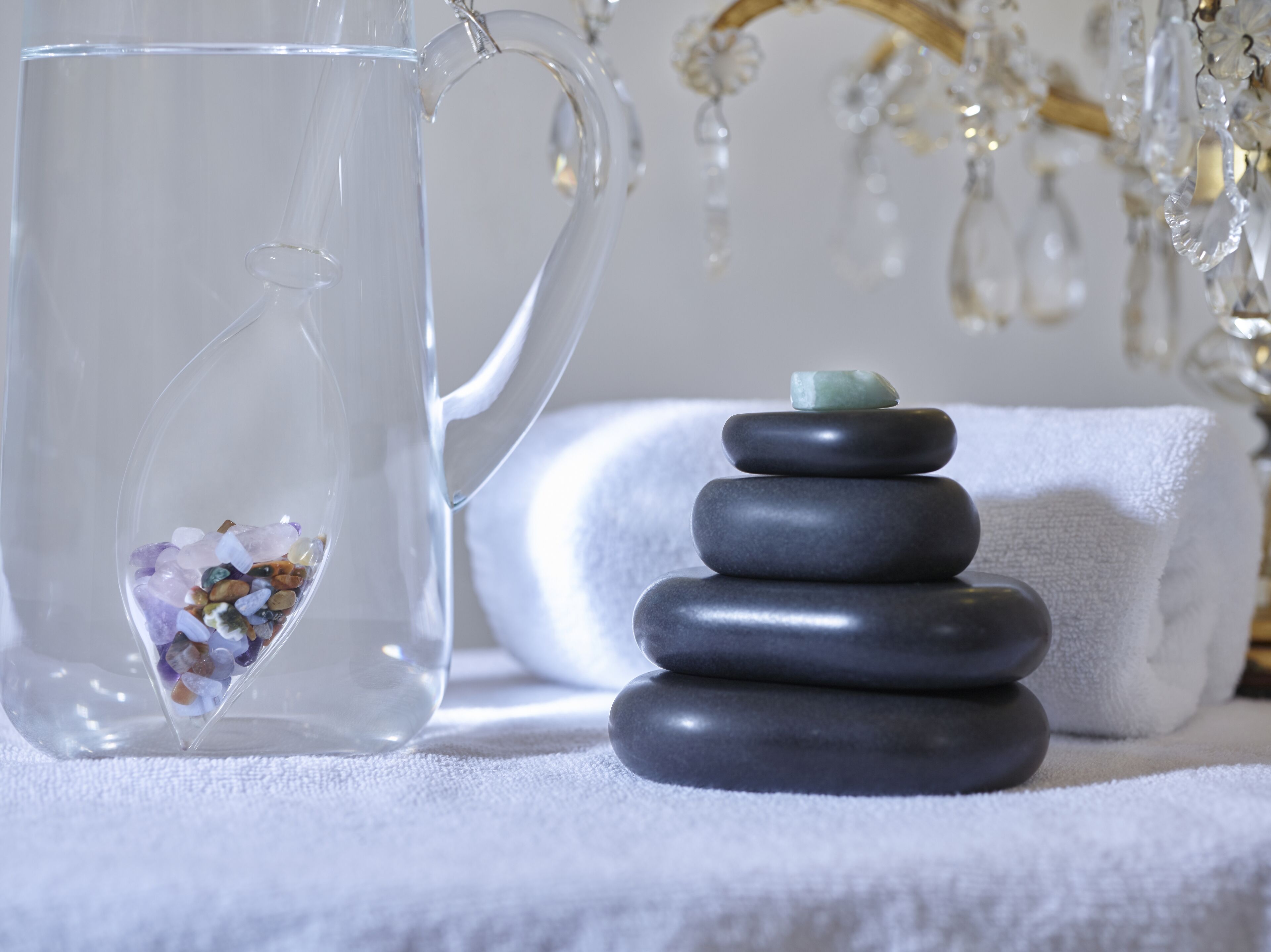 A clear glass pitcher filled with water and multicolored stones, a stack of smooth stones, and a white towel.