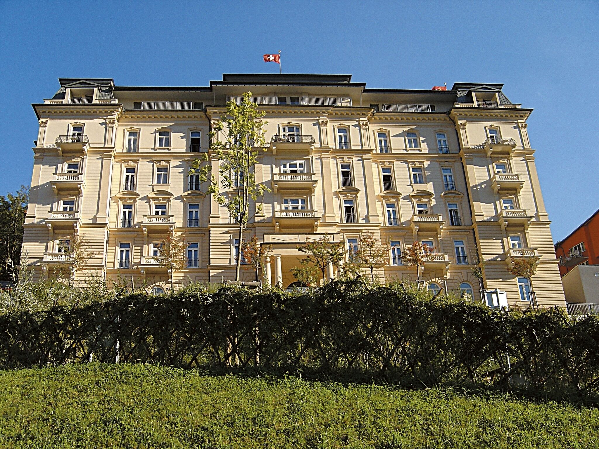 A multi-story building with a symmetrical facade, balconies, and a flag on top.