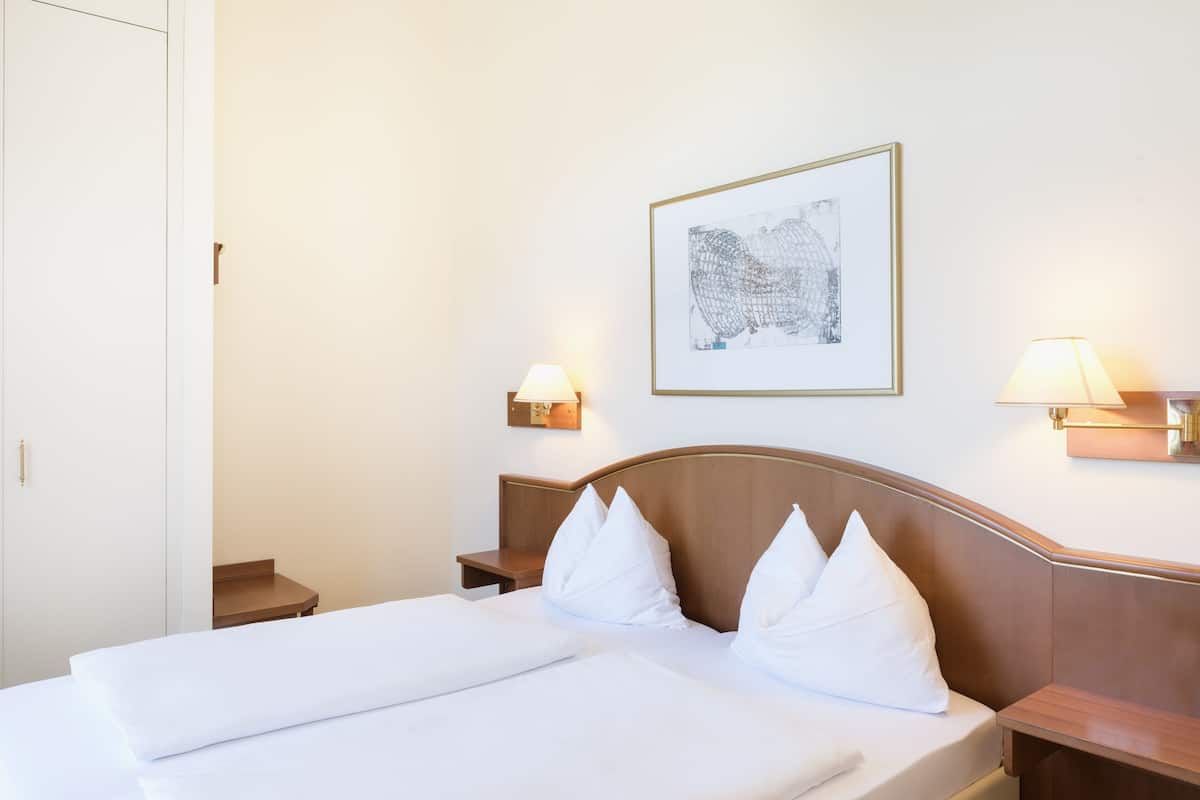 A hotel room with a bed, two bedside tables, and a wall-mounted lamp.