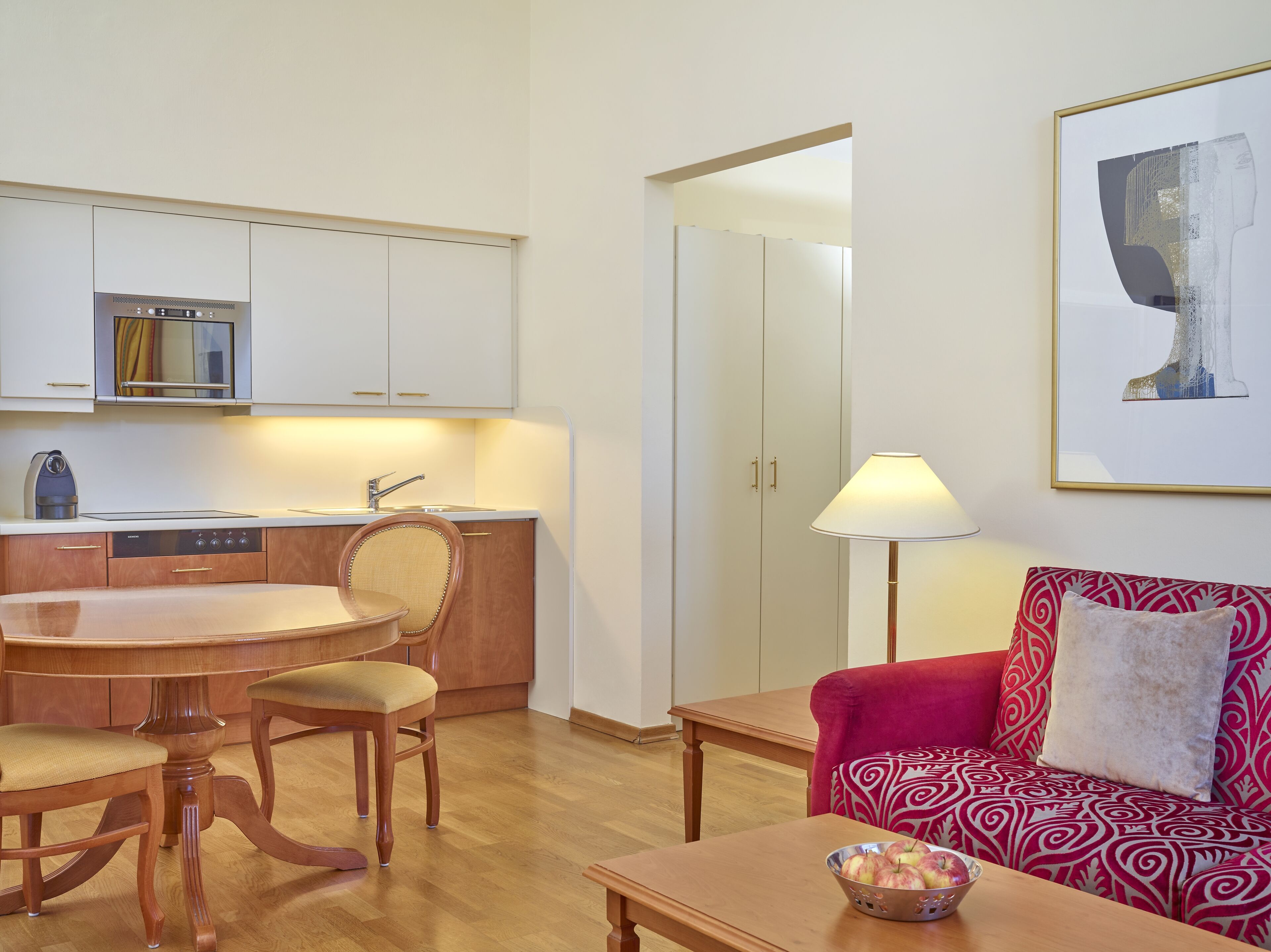 A compact living space with a kitchenette, dining area, and a red patterned sofa.