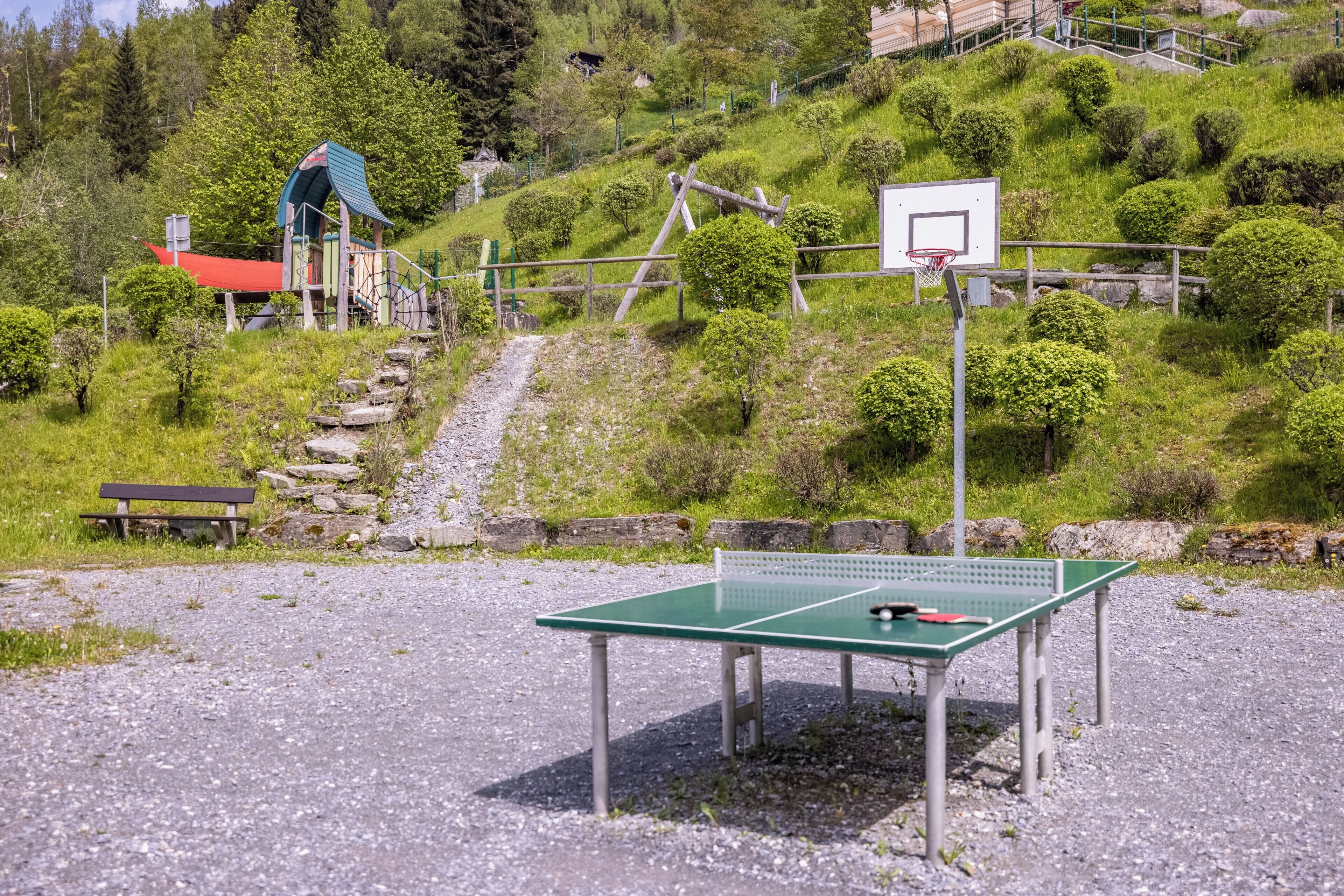 A ping pong table, a bench, and a basketball hoop in a park setting.