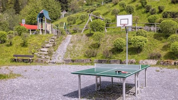 A ping pong table, a bench, and a basketball hoop in a park setting.