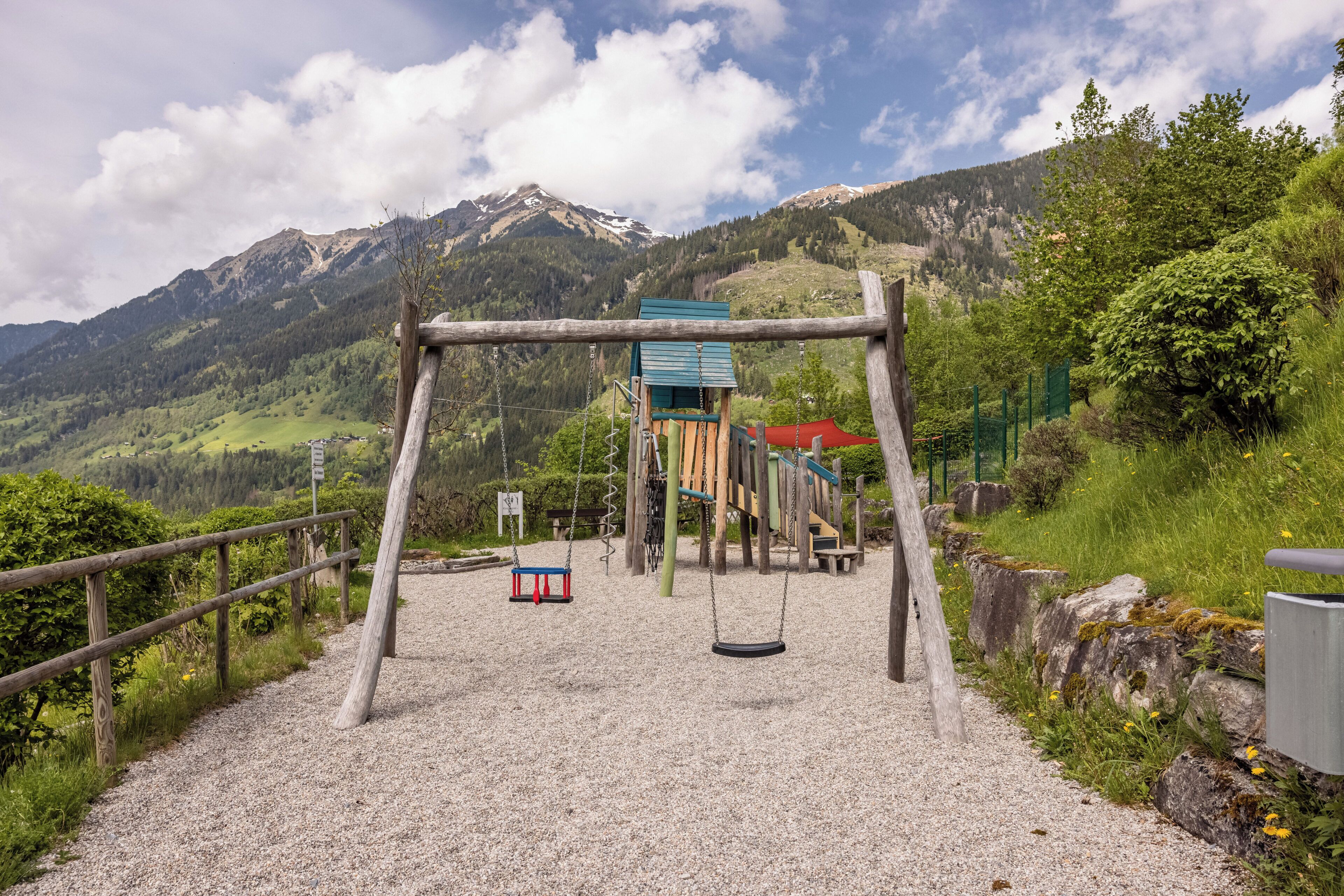 Un terrain de jeux avec des balançoires et une structure d’escalade, le tout situé dans un cadre montagneux.