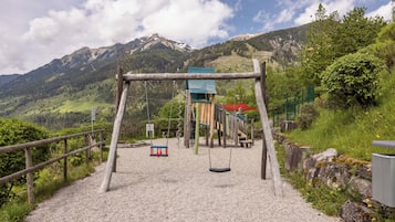 A playground with swings and a climbing structure, set against a mountainous backdrop.