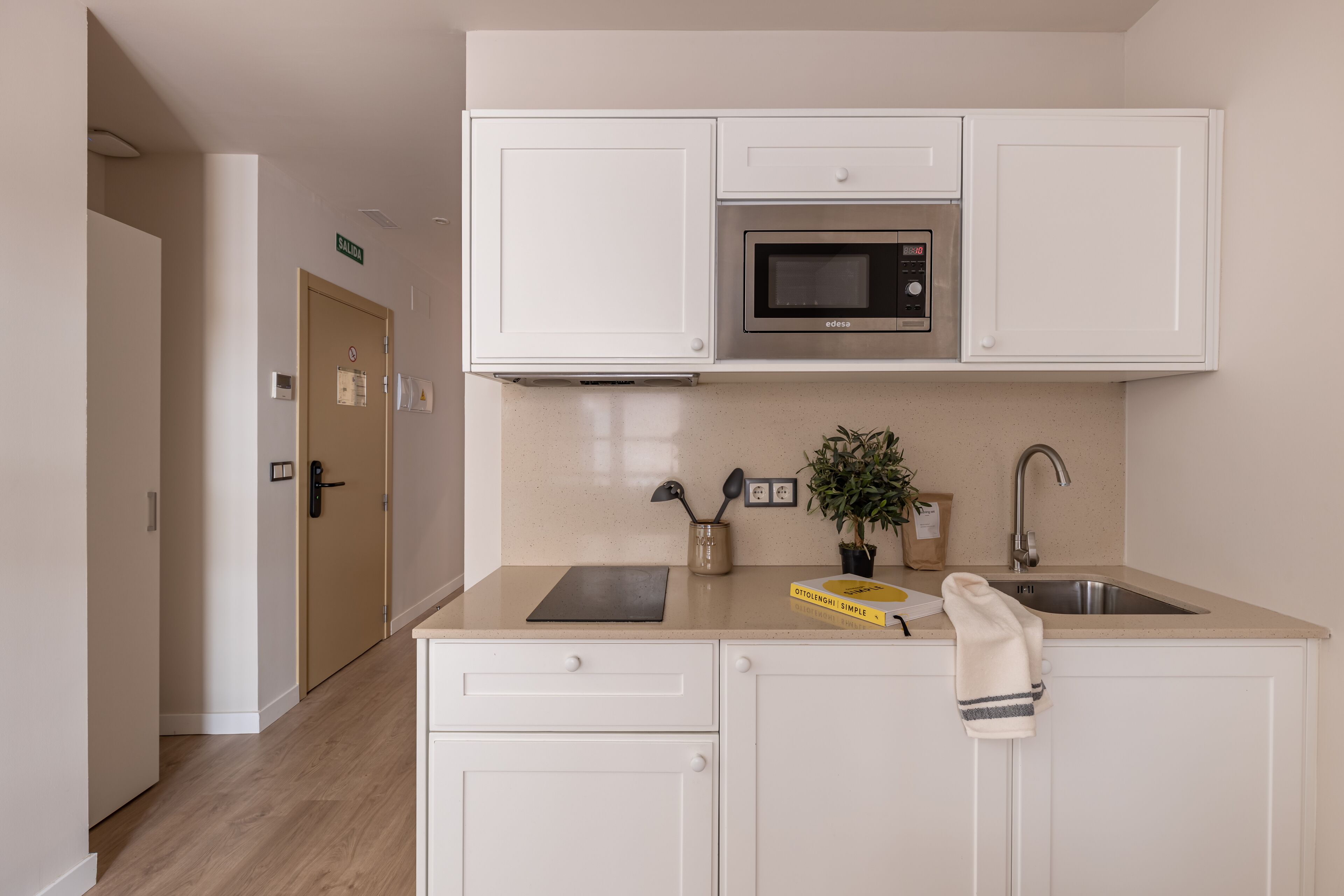 A modern kitchen with white cabinets, a microwave, a sink, and a countertop with a plant and a book.