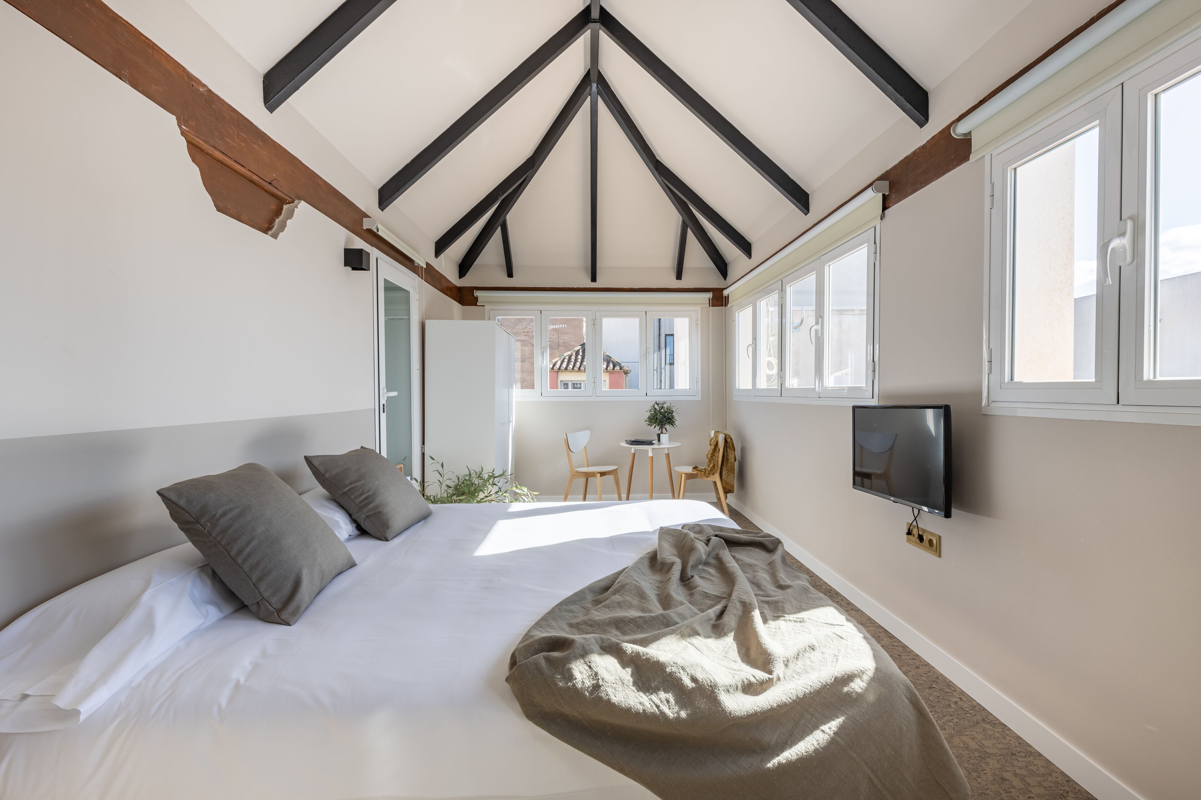 A bedroom with a large bed, a TV, and a window with a view of the outside.