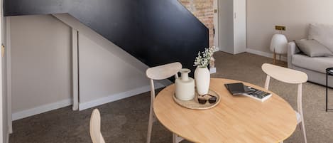A modern interior with a wooden dining table, chairs, a staircase with a black accent, and a hanging light fixture.