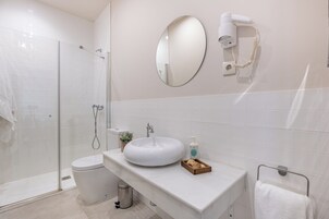 Et badeværelse med brusekabine i glas, toilet, vask med spejl, hårtørrer og håndklæderække.