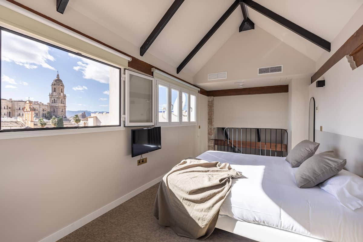 Een slaapkamer met een groot raam, een bed, een televisie en uitzicht op een historisch gebouw.