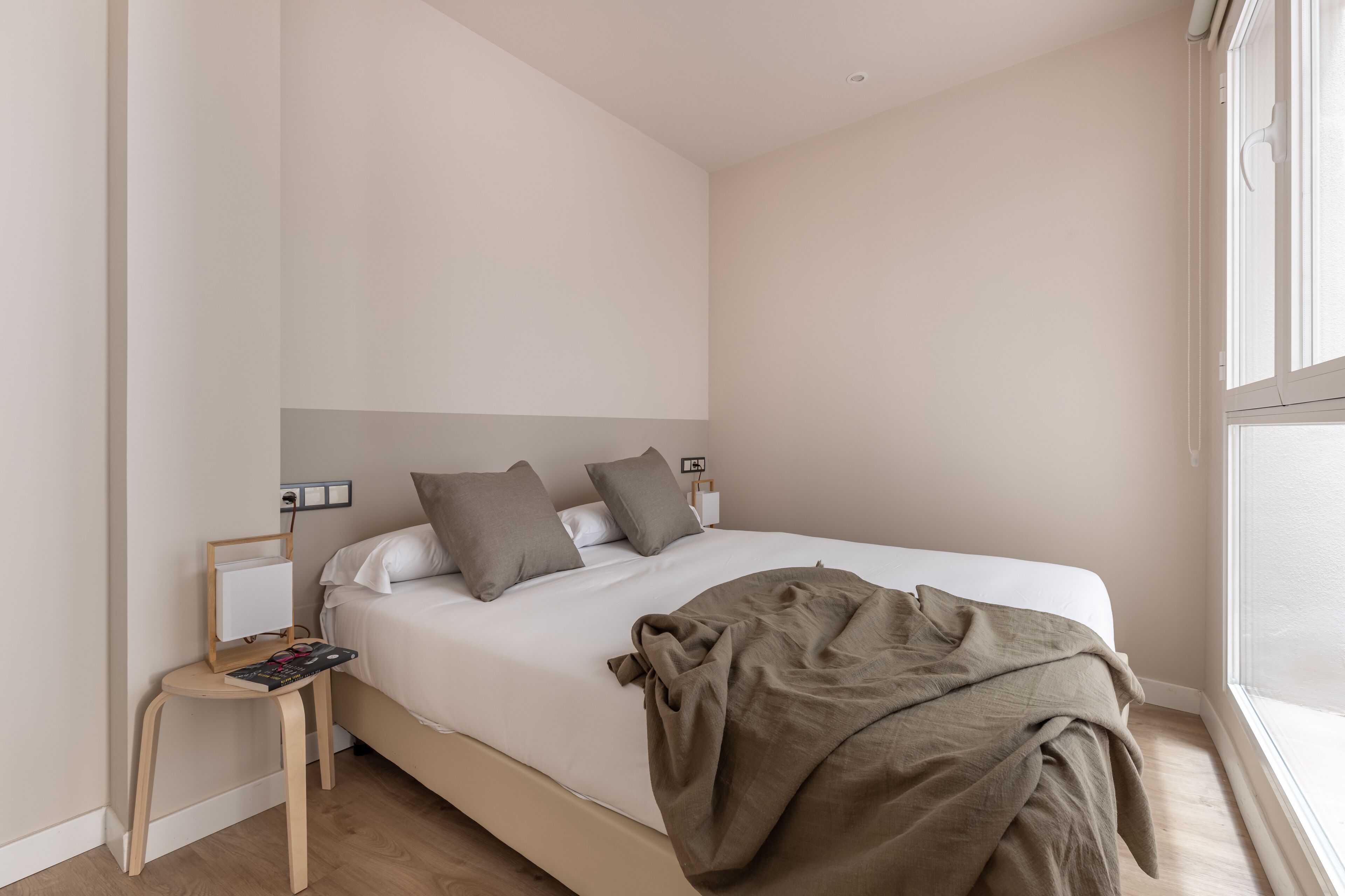 A bedroom with a bed, a bedside table, a lamp, and a window.