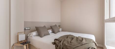 A bedroom with a bed, a bedside table, a lamp, and a window.