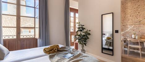 Una habitación de hotel con dos camas, un ventanal grande, un muro de ladrillo y un escritorio con una silla.