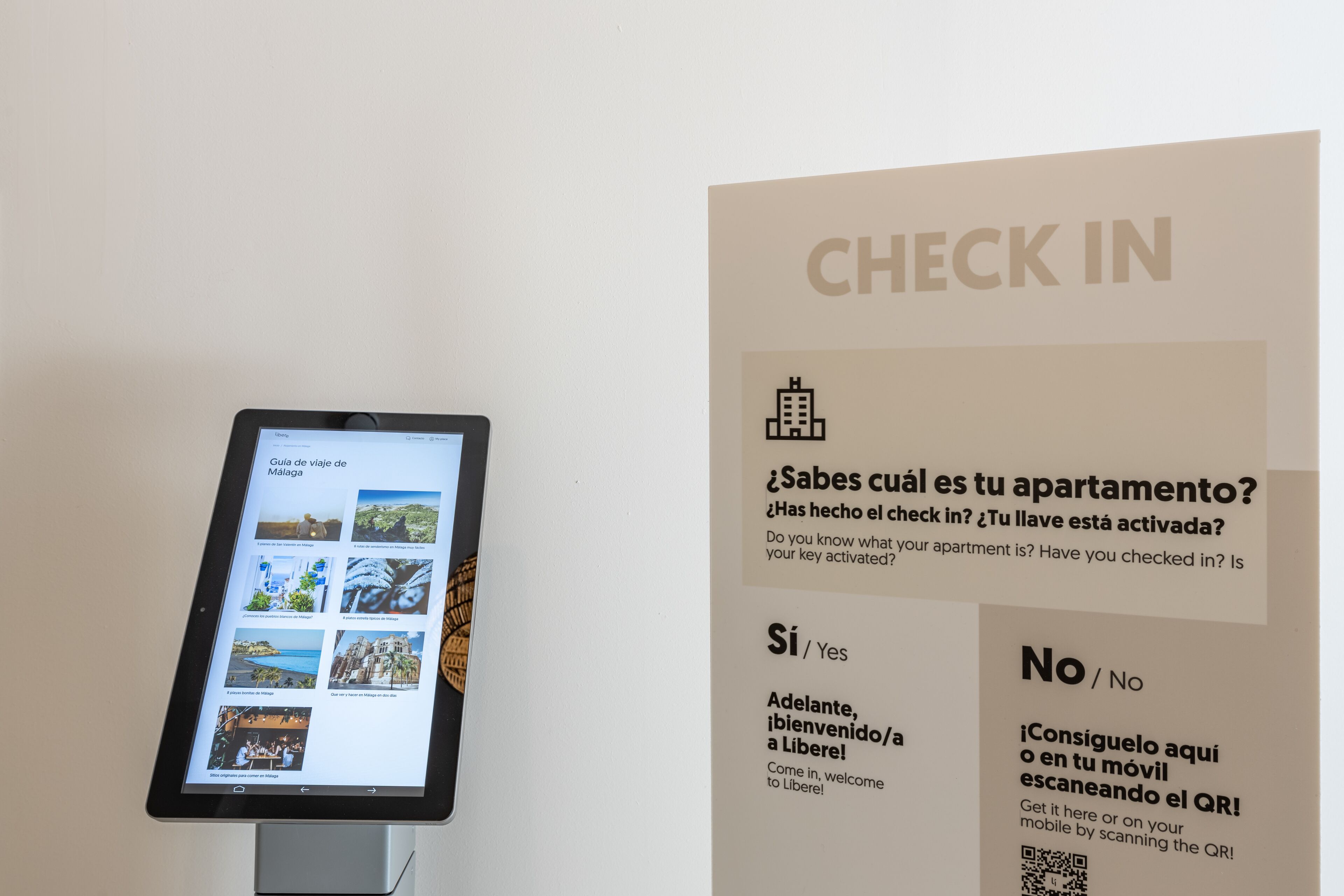 Een digitaal tablet waarop een reisgids voor Málaga staat, met een QR-code en een bord met instructies voor inchecken.
