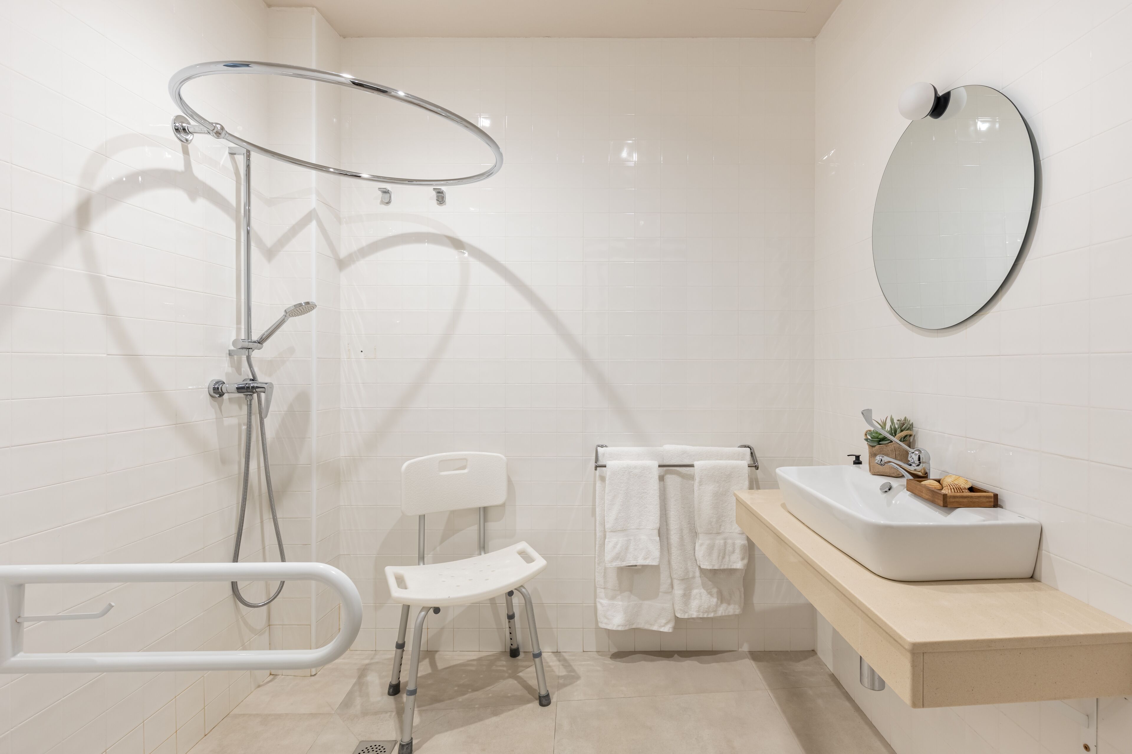 Un baño moderno con ducha, una silla blanca, un lavabo con espejo y un perchero para toallas.