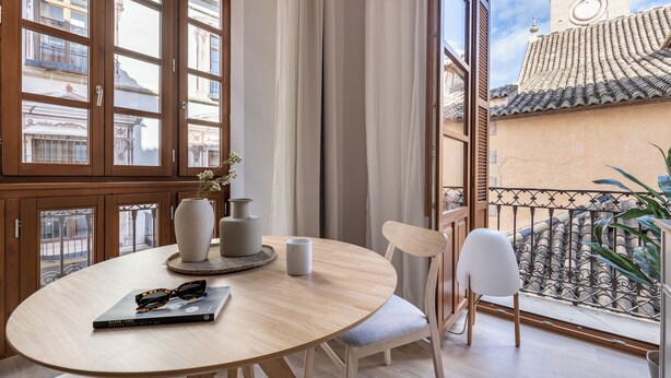 A round table with a book, a vase, and a mug. There are two chairs and a window with curtains. - Líbere Málaga Teatro Romano (Málaga)