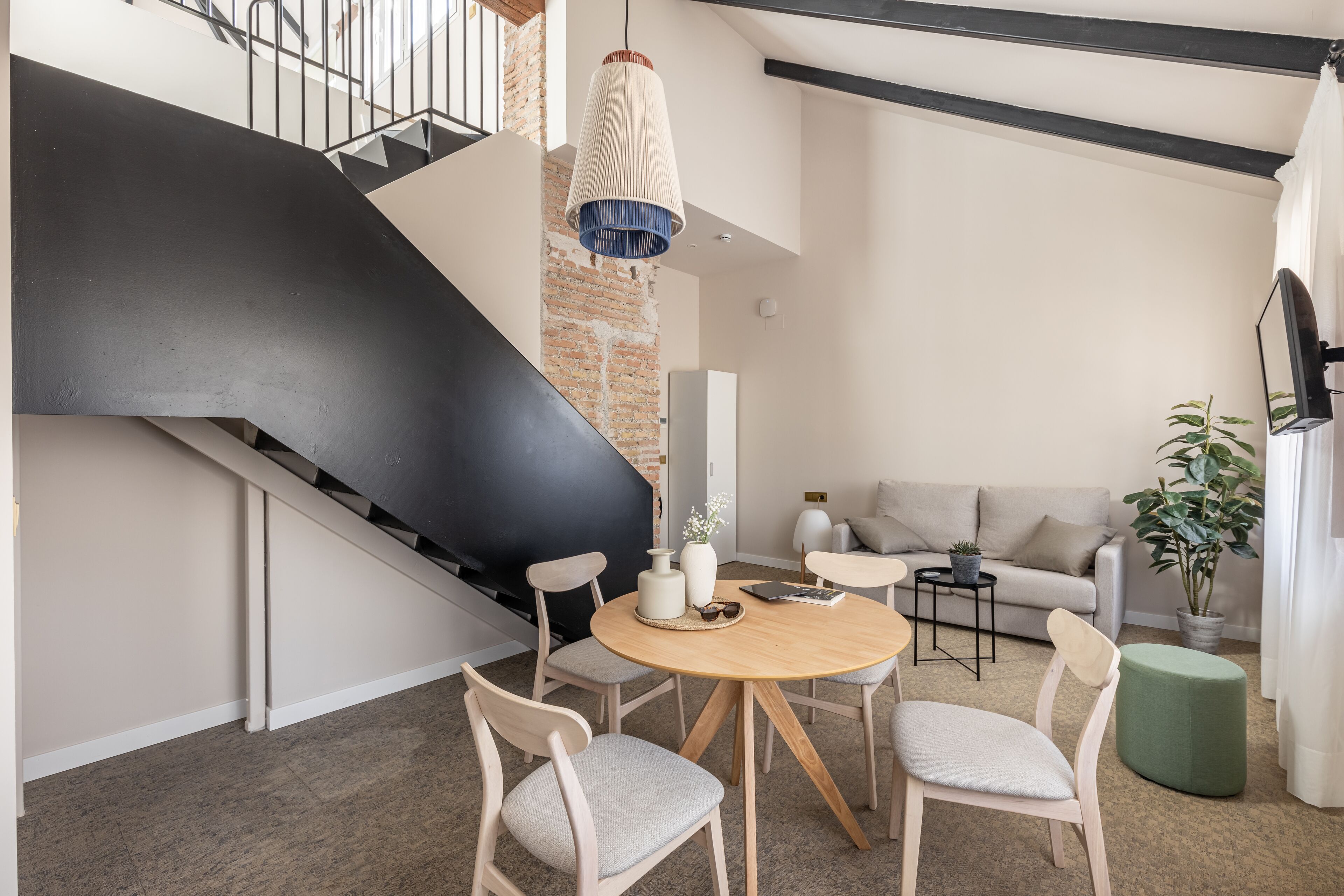 A modern living room with a staircase, a round wooden table, and a sofa.