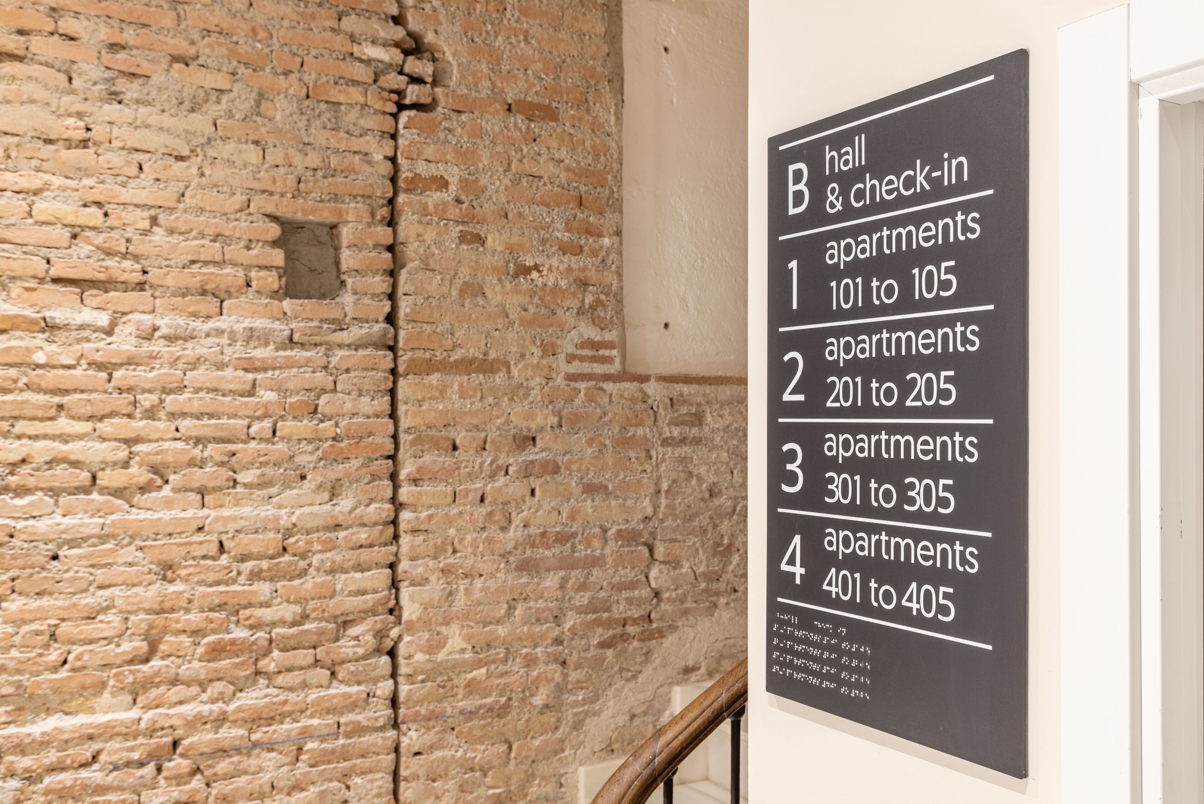 Une pancarte indiquant les numéros des appartements, de 101 à 405, dans un immeuble dont le mur de fond est en briques.