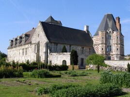 Um edifício histórico de pedra com um amplo jardim na frente.